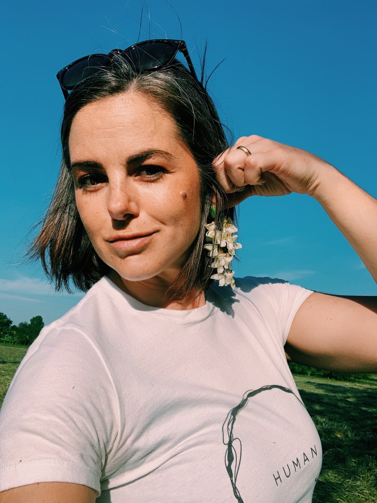 Woman holding black locust flower cluster next to ear as a pretend earings